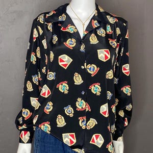 May include: A black silk blouse with a button-up front and long sleeves. The blouse features a repeating pattern of colorful crests and shields.