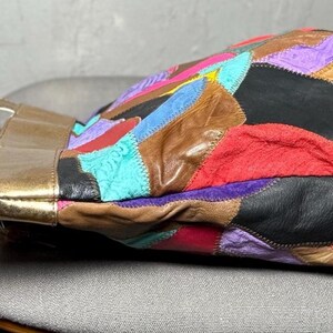 Peut inclure: Un sac &agrave; main en cuir patchwork multicolore avec des poign&eacute;es dor&eacute;es. Le sac pr&eacute;sente une vari&eacute;t&eacute; de couleurs, dont le rouge, le rose, le violet, le noir, le marron et le turquoise. Le sac est pos&eacute; sur une surface grise.