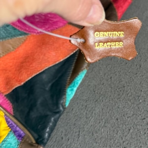 Peut inclure: Un article en cuir multicolore avec un motif patchwork. Une &eacute;tiquette en cuir marron porte l'inscription "GENUINE LEATHER" en lettres dor&eacute;es. Les couleurs incluent le rose, l'orange, le turquoise et le marron.