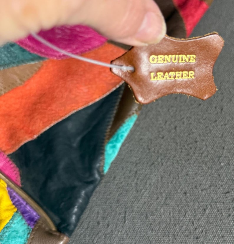Peut inclure: Un article en cuir multicolore avec un motif patchwork. Une &eacute;tiquette en cuir marron porte l'inscription "GENUINE LEATHER" en lettres dor&eacute;es. Les couleurs incluent le rose, l'orange, le turquoise et le marron.