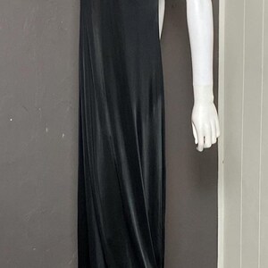 K&ouml;nnte beinhalten: Ein bodenlanges schwarzes Kleid auf einer Schaufensterpuppe. Das Kleid hat ein plissiertes Oberteil und Spaghettitr&auml;ger. Eine goldfarbene Halskette schm&uuml;ckt den Hals der Schaufensterpuppe. Das Kleid ist aus flie&szlig;endem, seidigem Material.