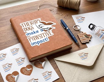 May include: A collection of items with the theme "Therapy Dogs make a PAWSITIVE impact!" includes a brown journal with a sticker, stickers, a pen, a keychain, a water bottle, and an envelope. The items are arranged on a wooden surface.