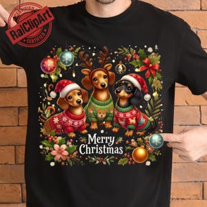 May include: Black t-shirt featuring three dachshunds dressed in Christmas sweaters and Santa hats. The dogs are surrounded by festive decorations and the words "Merry Christmas".