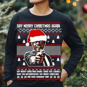 May include: Black long-sleeve shirt with a Christmas sweater design. The shirt features a graphic of a man wearing a Santa hat, holding a gun, and the text "SAY MERRY CHRISTMAS AGAIN." The design includes Christmas trees and snowflakes.