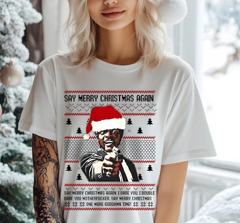 May include: White t-shirt with a humorous Christmas design. The graphic features a man wearing a Santa hat, holding a gun, and the text "SAY MERRY CHRISTMAS AGAIN." The design includes Christmas trees and a repeating text pattern.