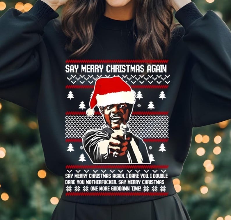May include: Black sweatshirt with a Christmas-themed design. The design features a man wearing a Santa hat and holding a gun, with the text "SAY MERRY CHRISTMAS AGAIN." Additional text includes "I dare you...Say Merry Christmas...One more goddamn time!"