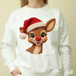 May include: White sweatshirt featuring a cartoon reindeer wearing a Santa hat. The reindeer has a red nose, brown fur, and large eyes. The hat is red and white, and the design is centered on the front of the sweatshirt. A festive holiday-themed apparel item.