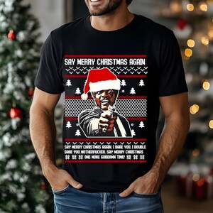 May include: Black t-shirt with a Christmas sweater design. The design features a man wearing a Santa hat, holding a gun, and the text "SAY MERRY CHRISTMAS AGAIN." Additional text reads "I dare you... one more goddamn time!"