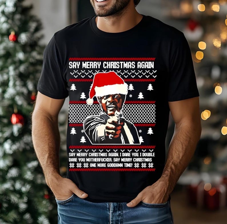 May include: Black t-shirt with a Christmas sweater design. The design features a man wearing a Santa hat, holding a gun, and the text "SAY MERRY CHRISTMAS AGAIN." Additional text reads "I dare you... one more goddamn time!"