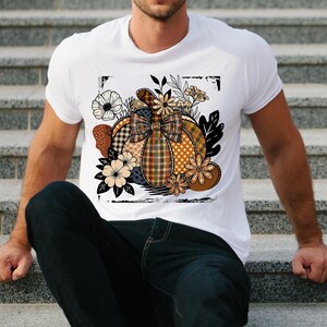 Peut inclure: T-shirt blanc avec un motif de citrouille en patchwork. La citrouille présente un nœud à carreaux, des pois et des motifs floraux. Le motif comprend des feuilles et des fleurs dans les tons de marron, d'orange et de crème. Le motif est encadré d'un cadre noir vieilli.