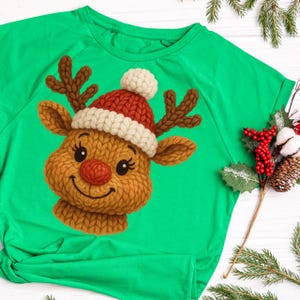 Peut inclure: T-shirt vert vif avec un motif de visage de renne tricoté. Le renne a un nez rouge, des bois bruns et un bonnet tricoté rouge et blanc. Le design est sur le thème des fêtes, parfait pour Noël.
