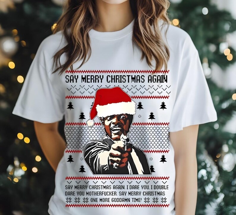 May include: White t-shirt with a Christmas-themed graphic. The design features a man wearing a Santa hat, holding a gun, and the text "SAY MERRY CHRISTMAS AGAIN." Additional text at the bottom reads "ONE MORE GODDAMN TIME!"