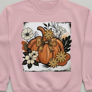 Peut inclure: Sweat-shirt rose clair avec un motif sur le thème de l'automne. Le motif comprend une citrouille orange avec un nœud, entourée de fleurs et de feuilles. Le design est encadré dans un carré blanc avec un bord vieilli.