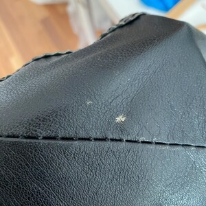 K&ouml;nnte beinhalten: Nahaufnahme einer schwarzen Ledertasche. Das Leder hat eine strukturierte Oberfl&auml;che mit sichtbaren N&auml;hten und einem dekorativen Rand. Die Tasche scheint neu zu sein, mit ein paar kleinen Unvollkommenheiten auf der Oberfl&auml;che.