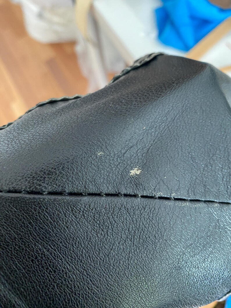 K&ouml;nnte beinhalten: Nahaufnahme einer schwarzen Ledertasche. Das Leder hat eine strukturierte Oberfl&auml;che mit sichtbaren N&auml;hten und einem dekorativen Rand. Die Tasche scheint neu zu sein, mit ein paar kleinen Unvollkommenheiten auf der Oberfl&auml;che.