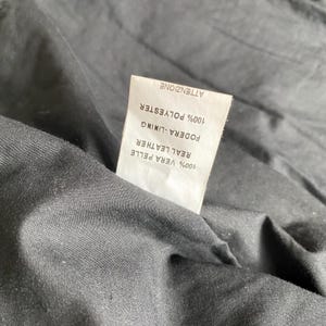 K&ouml;nnte beinhalten: Nahaufnahme des Inneren eines schwarzen Kleidungsst&uuml;cks mit einem wei&szlig;en Etikett. Das Etikett gibt an, dass das Futter aus 100 % Polyester und das Echtleder aus 100 % Vera Pelle besteht. Das Wort "ATTENZIONE" ist ebenfalls sichtbar.
