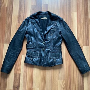 K&ouml;nnte beinhalten: Schwarze Lederjacke mit Reverskragen, Knopfverschluss und mehreren Taschen. Die Jacke hat eine taillierte Silhouette und ein klassisches Design. Die Jacke ist aus glattem, gl&auml;nzendem Leder gefertigt. Ein vielseitiges Kleidungsst&uuml;ck f&uuml;r jede Garderobe.