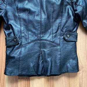 K&ouml;nnte beinhalten: Schwarze Lederjacke mit tailliertem Schnitt. Zu den Merkmalen geh&ouml;ren ein Reverskragen, aufgesetzte Taschen mit Kn&ouml;pfen und detaillierte N&auml;hte. Die Jacke hat ein klassisches, zeitloses Design.
