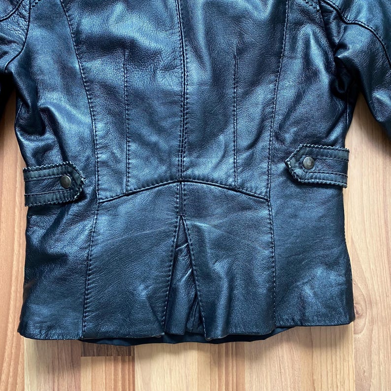 K&ouml;nnte beinhalten: Schwarze Lederjacke mit tailliertem Schnitt. Zu den Merkmalen geh&ouml;ren ein Reverskragen, aufgesetzte Taschen mit Kn&ouml;pfen und detaillierte N&auml;hte. Die Jacke hat ein klassisches, zeitloses Design.