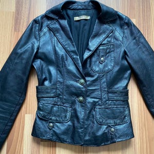 K&ouml;nnte beinhalten: Schwarzer Lederblazer mit Reverskragen, zwei Vordertaschen und zwei Brusttaschen. Die Jacke hat einen Knopfverschluss und dekorative N&auml;hte. Ein klassischer Stil.
