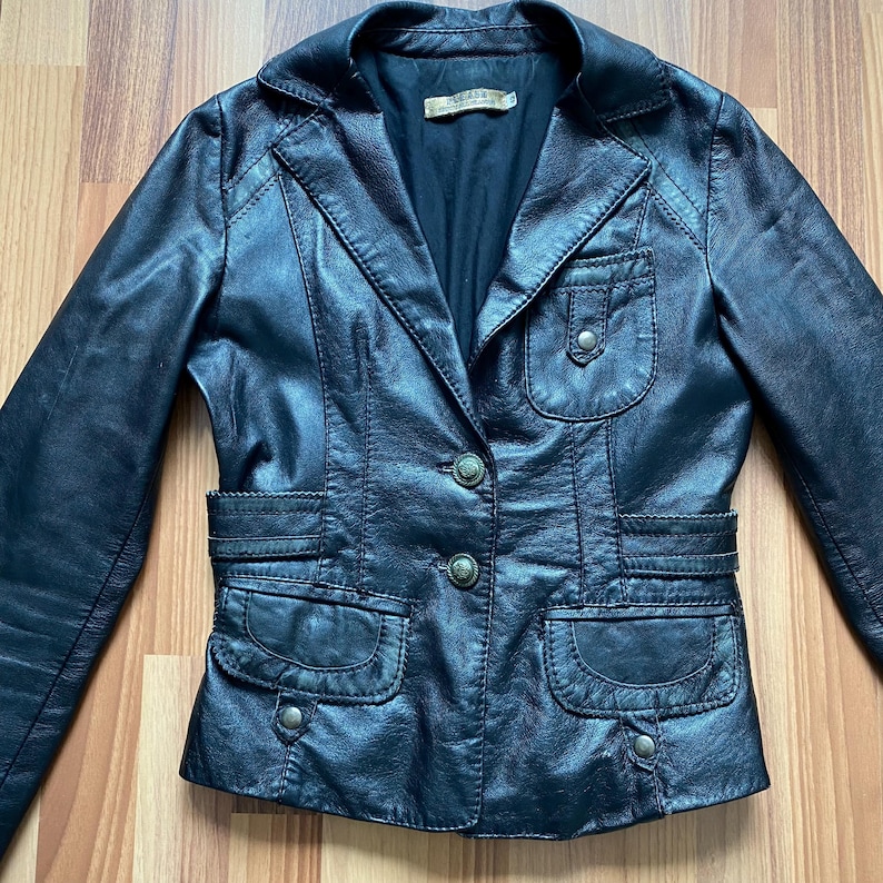 K&ouml;nnte beinhalten: Schwarzer Lederblazer mit Reverskragen, zwei Vordertaschen und zwei Brusttaschen. Die Jacke hat einen Knopfverschluss und dekorative N&auml;hte. Ein klassischer Stil.