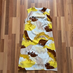 Könnte beinhalten: Ärmelloses Vintage-Kleid mit einem Muster aus gelben, braunen und weißen wellenförmigen Formen. Das Kleid hat einen Rundhalsausschnitt und einen geraden, knielangen Schnitt und zeigt eine Retro-Ästhetik.