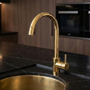 May include: A polished gold-toned kitchen faucet with a high-arc spout and a single side-mounted lever handle, paired with a matching circular gold-toned basin sink set into a dark black marble countertop with subtle white veining throughout.