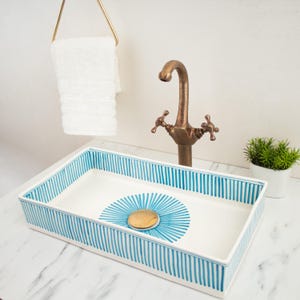 May include: A white ceramic bathroom sink with a blue and white striped design. The sink has a circular, blue and white design in the centre. A brass faucet is mounted above the sink.
