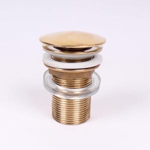 May include: A gold-toned pop-up drain stopper for a sink or bath. The stopper has a round top and a threaded base. It includes a white rubber seal and a clear plastic washer.