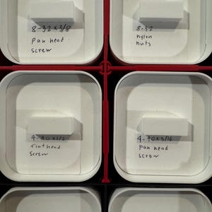 Puede incluir: Primer plano de un contenedor de almacenamiento con m&uacute;ltiples compartimentos blancos. Cada compartimento contiene peque&ntilde;os art&iacute;culos de ferreter&iacute;a y etiquetas manuscritas. Las etiquetas incluyen texto como "8-32 x 3/8 pan head screw" y "4-40 x 1/2 flat head screw."