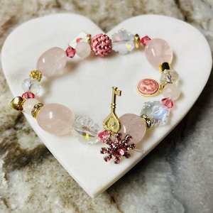 Esta pulsera de San Valentín de 10" incluye un dije en forma de camafeo rosa en miniatura, un dije en forma de llave con joyas, un botón de diamantes de imitación rosas y un dije en forma de carta de amor. ¡Impresionante!