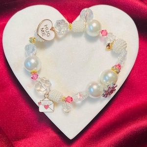 "Dieses zarte pinke 25cm Armband ist mit einem ""Hug Me"" Herz, einem rosa Strassstein und einem Liebesbrief Charm verziert - Perfekt zum Valentinstag!"