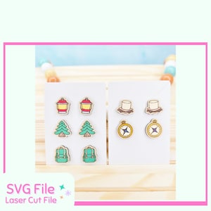 May include: Wooden earrings featuring camping-themed designs. The earrings include images of lanterns, pine trees, backpacks, compasses, and hats. The earrings are displayed on white cards against a light wood background. The text "SVG File Laser Cut File" is visible.