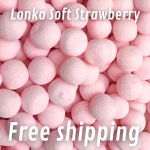 Può includere: Primo piano di molte caramelle rotonde rosa chiaro. Le caramelle sono sparse e riempiono l'inquadratura. Il testo "Lonka Soft Strawberry" è in alto e "Free shipping" in basso.