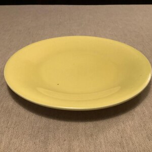 Pu&ograve; includere: Un piatto rotondo giallo chiaro con un bordo leggermente rialzato. Il piatto &egrave; di un colore giallo pallido uniforme e sembra essere fatto di ceramica o materiale simile. &Egrave; centrato su una superficie dai toni neutri.