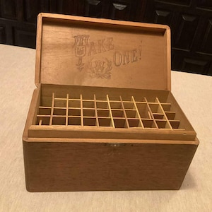 May include: A wooden box with a hinged lid and a compartmentalized interior. The lid has the text "Take One!" printed on it.
