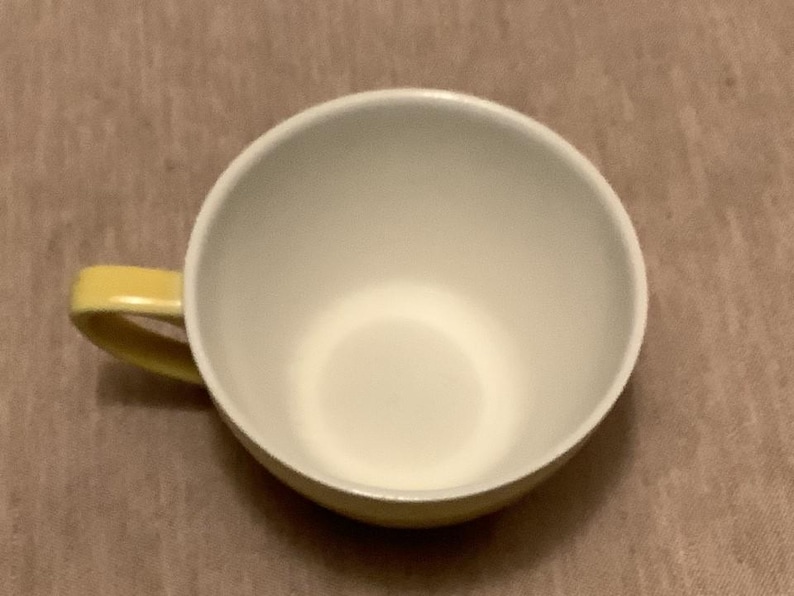 Pu&ograve; includere: Una tazza da t&egrave; in ceramica bianca con manico giallo. La tazza ha un'ampia apertura e una base arrotondata. L'interno &egrave; bianco e l'esterno &egrave; giallo pallido. La tazza &egrave; appoggiata su una superficie marrone.