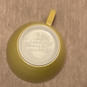 Pu&ograve; includere: Vista dall'alto di una tazza da t&egrave; gialla con manico. L'interno della tazza &egrave; bianco e il fondo riporta la scritta "VILLEROY & BOCH MADE IN LUXEMBOURG". La tazza &egrave; su una superficie beige.