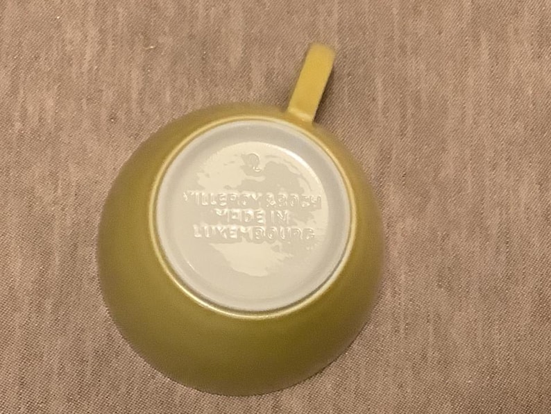 Pu&ograve; includere: Vista dall'alto di una tazza da t&egrave; gialla con manico. L'interno della tazza &egrave; bianco e il fondo riporta la scritta "VILLEROY & BOCH MADE IN LUXEMBOURG". La tazza &egrave; su una superficie beige.