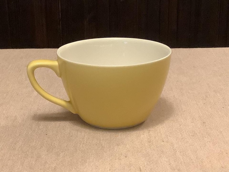 Pu&ograve; includere: Una tazza da t&egrave; in ceramica gialla con interno bianco. La tazza ha una forma arrotondata e un manico curvo. La tazza da t&egrave; &egrave; su una superficie di colore chiaro, con uno sfondo marrone scuro.
