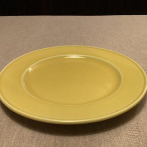 Pu&ograve; includere: Un piatto rotondo in ceramica gialla con un bordo leggermente rialzato. Il piatto ha una finitura liscia e lucida ed &egrave; posto su uno sfondo neutro. Questo piatto &egrave; adatto per servire i pasti.