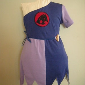 May include: A purple and blue dress with a black and red embroidered symbol on the chest. The dress has a white trim and a tie at the waist.