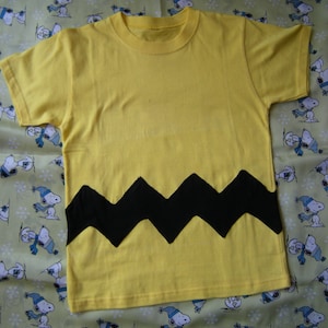 May include: A yellow t-shirt with a black zig-zag pattern across the bottom.