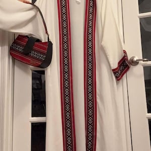 May include: A white long-sleeved cardigan with red and black geometric patterned trim. A small red and black patterned handbag is included.