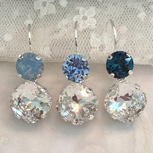 May include: Three pairs of drop earrings featuring silver-toned hooks. Each earring has a small round crystal at the top in varying shades of blue, paired with a larger, faceted clear crystal at the bottom held in a silver-toned metal setting.