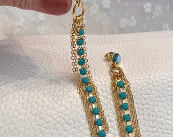 May include: Gold-toned earrings with turquoise-colored stones and chain fringe. The earrings have a post backing and a small turquoise stone on the post. The chain fringe is made of multiple strands of delicate gold chains.