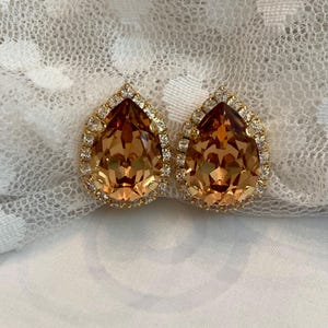 May include: A pair of gold tone teardrop earrings with a large amber colored crystal surrounded by smaller clear crystals.
