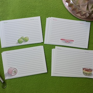 May include: Recipe cards with lined pages and illustrated food images. A wooden spoon and whisk are on the left. The cards have illustrations of limes, a cake stand, a roll, and a layered dessert. The background is green.