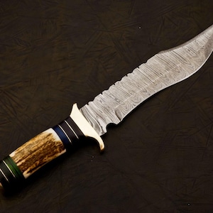 May include: A large, ornate hunting knife with a Damascus steel blade and a handle made of antler, wood, and black and blue accents. The blade has a serrated edge near the handle and a curved tip. The knife is set against a dark background.