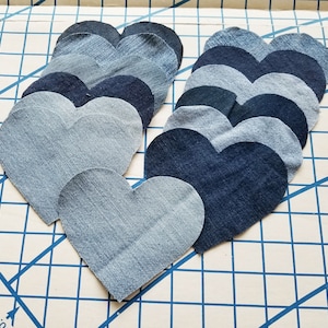 May include: A stack of denim heart shapes in various shades of blue, arranged in a graduated pattern from light to dark. The hearts are layered on top of each other, creating a visually appealing and textured design.